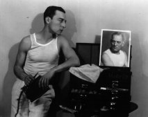 American comic actor Buster Keaton (1895 - 1966) originally Joseph Francis Keaton, engages in a staring match with a photograph of Lon Chaney as he prepares to apply his make-up. (Photo by Ruth Harriet Louise/Getty Images)